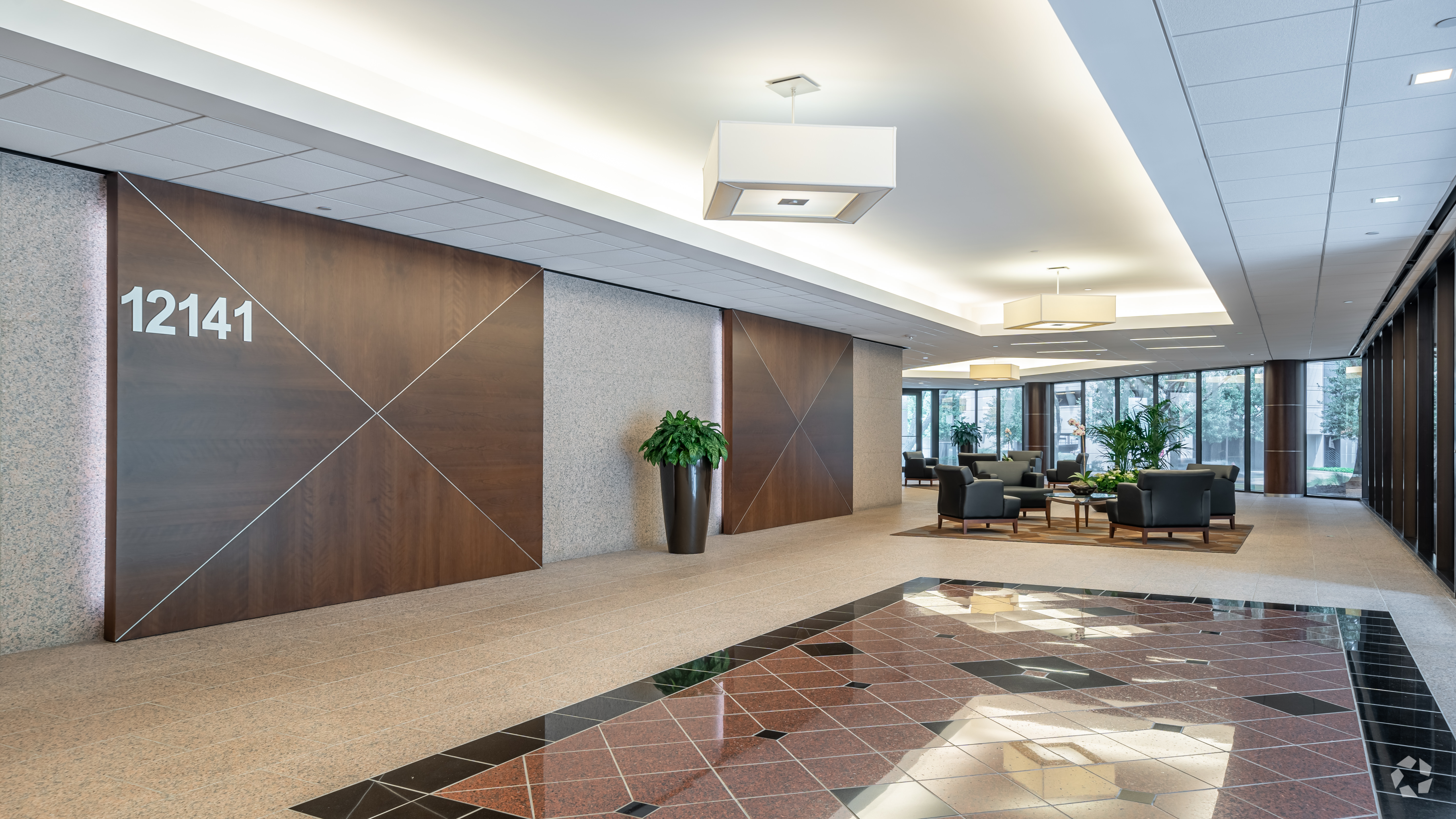 Modern office lobby with the number “12141” on a wooden wall panel, decorative lighting, potted plants, seating area with chairs and tables, and tiled flooring near the entrance.