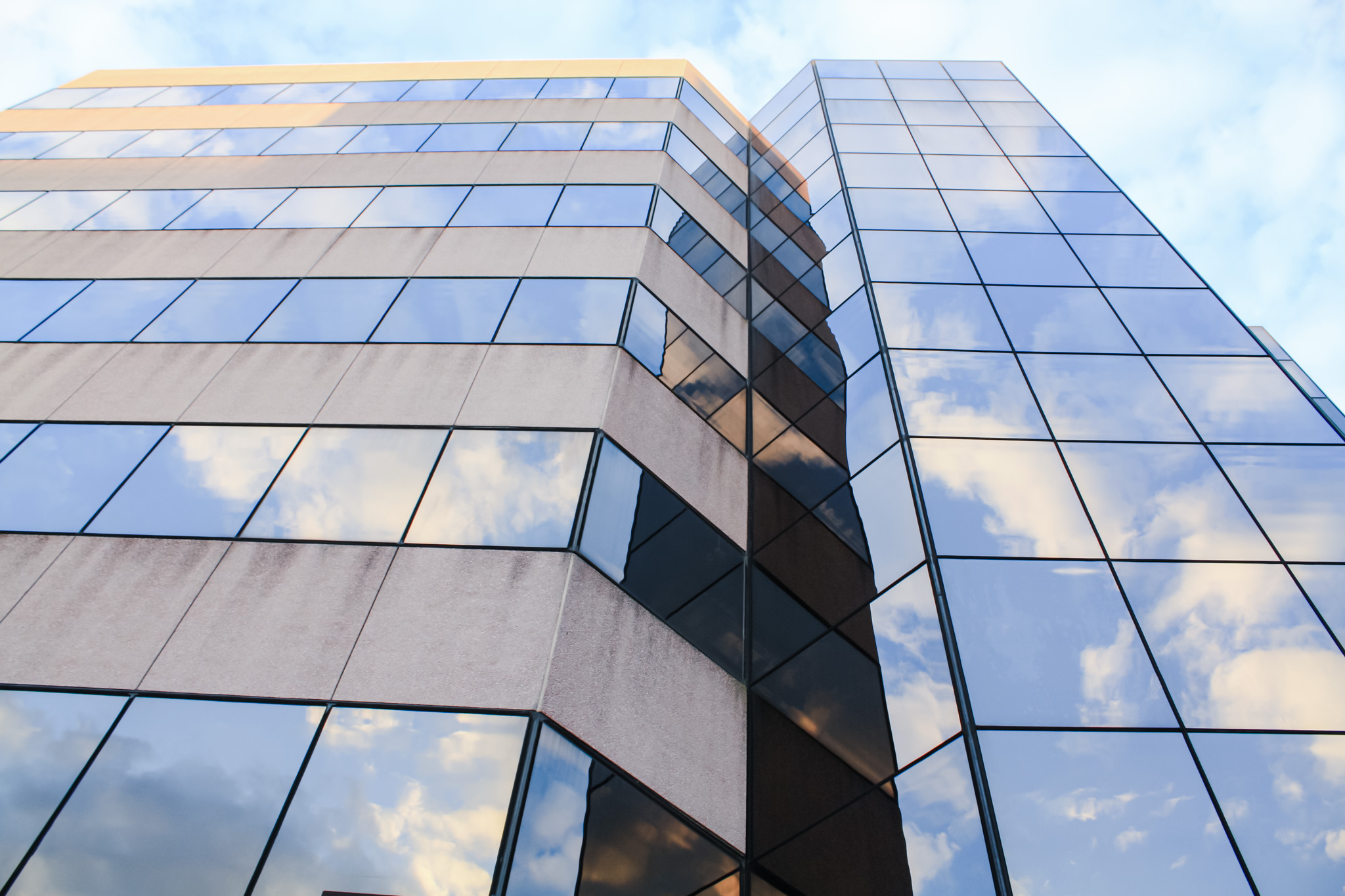 Close-up of a modern office building with a glass facade reflecting clouds and sky, featuring angular architectural design