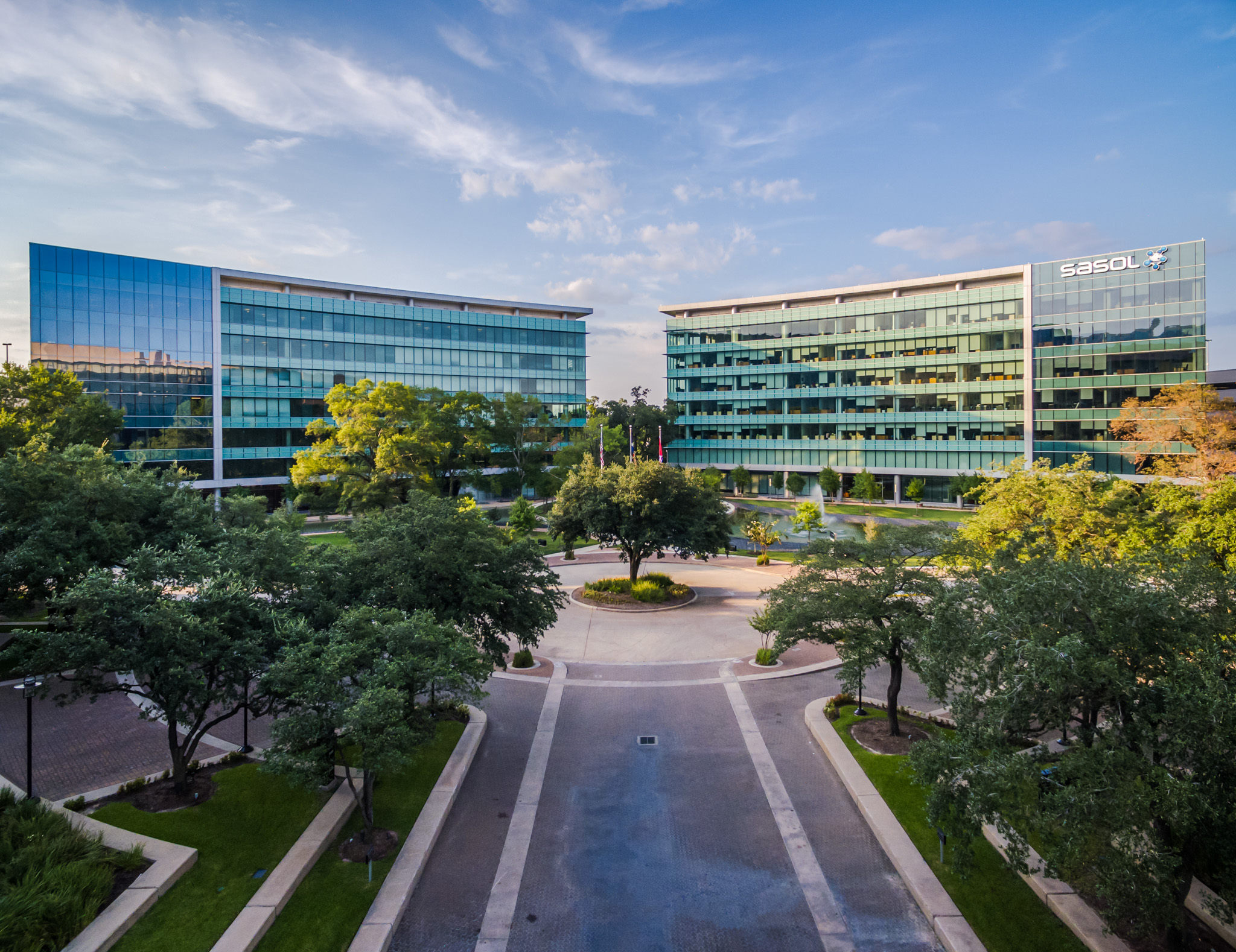 Two modern office buildings with glass facades facing each other, separated by a landscaped courtyard with trees and pathways.